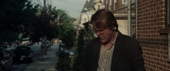 Movie still from “Synecdoche, New York” (2008), directed by Charlie Kaufman – A man wearing glasses and a jacket is standing outside; Medium shot, Over the shoulder angle