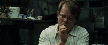 Movie still from “Synecdoche, New York” (2008), directed by Charlie Kaufman – A man with glasses is sitting in front of a table; Close Up shot, Over the shoulder angle