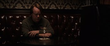 Movie still from “Synecdoche, New York” (2008), directed by Charlie Kaufman – A man sitting at a table with a drink in front of him; Medium shot, High angle