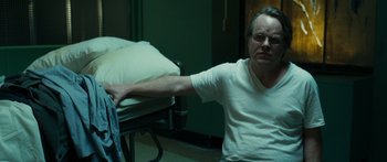 Movie still from “Synecdoche, New York” (2008), directed by Charlie Kaufman – A man sitting on the floor in front of a hospital bed; Medium shot, Over the shoulder angle