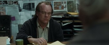 Movie still from “Synecdoche, New York” (2008), directed by Charlie Kaufman – A man sitting at a table in front of papers; Close Up shot, Over the shoulder angle