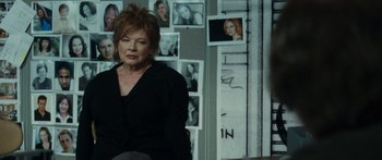 Movie still from “Synecdoche, New York” (2008), directed by Charlie Kaufman – An older woman sitting in front of a bunch of pictures; Medium shot, Over the shoulder angle