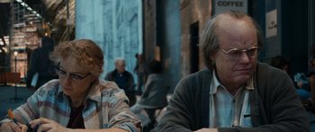 Movie still from “Synecdoche, New York” (2008), directed by Charlie Kaufman – A man and a woman sitting at a table in front of other people; Medium shot, Over the shoulder angle