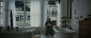 Movie still from “Synecdoche, New York” (2008), directed by Charlie Kaufman – A man sitting on a chair in front of a large window; Wide shot, Low angle