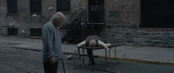 Movie still from “Synecdoche, New York” (2008), directed by Charlie Kaufman – A man laying on top of a table on the street; Wide shot, High angle