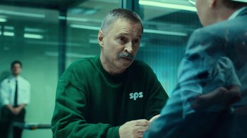 Movie still from “T2 Trainspotting” (2017), directed by Danny Boyle – A man in a green sweatshirt sitting in front of a window; Medium shot, Over the shoulder angle