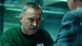 Movie still from “T2 Trainspotting” (2017), directed by Danny Boyle – An older man in a green t - shirt is sitting down; Close Up shot, Over the shoulder angle