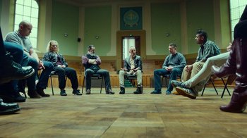 Movie still from “T2 Trainspotting” (2017), directed by Danny Boyle – A group of men sitting in a circle on chairs; Wide shot, High angle