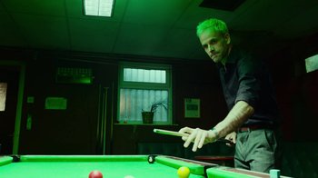 Movie still from “T2 Trainspotting” (2017), directed by Danny Boyle – A man is playing a game of pool in a green room; Medium shot, Over the shoulder angle