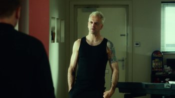Movie still from “T2 Trainspotting” (2017), directed by Danny Boyle – A man in a black tank top with a tattoo on his arm; Medium shot, Over the shoulder angle