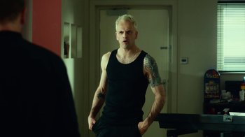 Movie still from “T2 Trainspotting” (2017), directed by Danny Boyle – A man in a black tank top with his hands in his pockets looking into a mirror; Medium shot, Over the shoulder angle