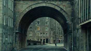 Movie still from “T2 Trainspotting” (2017), directed by Danny Boyle – A person is standing under an archway on a street; Extreme Wide shot, High angle
