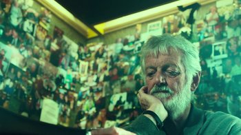 Movie still from “T2 Trainspotting” (2017), directed by Danny Boyle – An older man sitting in front of a wall covered in pictures; Close Up shot, Low angle