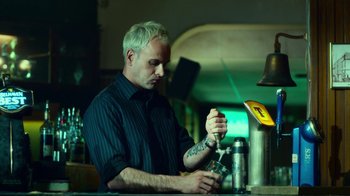 Movie still from “T2 Trainspotting” (2017), directed by Danny Boyle – A man sitting at a table with a drink in his hand; Medium shot, Low angle