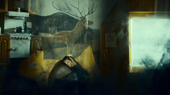 Movie still from “T2 Trainspotting” (2017), directed by Danny Boyle – A man is standing in front of a painting of a deer; Wide shot, High angle