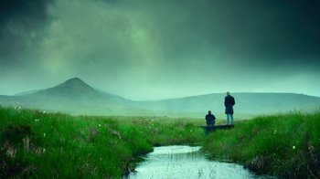 Movie still from “T2 Trainspotting” (2017), directed by Danny Boyle – Two people standing in a grassy field near a river; Extreme Wide shot, Low angle