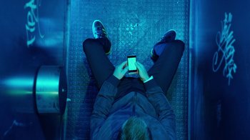 Movie still from “T2 Trainspotting” (2017), directed by Danny Boyle – A man sitting on the ground looking at his cell phone; Wide shot, Overhead angle