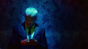 Movie still from “T2 Trainspotting” (2017), directed by Danny Boyle – A man in a suit and tie looking at a cell phone; Close Up shot, Overhead angle