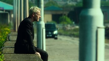 Movie still from “T2 Trainspotting” (2017), directed by Danny Boyle – A man sitting on top of a cement wall; Medium shot, Low angle