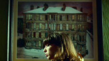 Movie still from “T2 Trainspotting” (2017), directed by Danny Boyle – A woman standing in front of a painting of a building; Medium shot, Over the shoulder angle