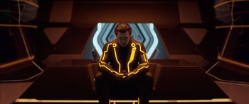 Movie still from “TRON: Legacy” (2010), directed by Joseph Kosinski – A man sitting on a chair wearing a yellow and black suit; Medium shot, Low angle