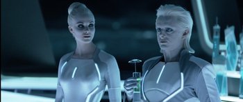 Movie still from “TRON: Legacy” (2010), directed by Joseph Kosinski – A couple of women standing next to each other holding a drink; Medium shot, Over the shoulder angle