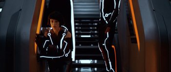 Movie still from “TRON: Legacy” (2010), directed by Joseph Kosinski – A woman standing next to a man wearing a neon suit; Medium shot, Over the shoulder angle