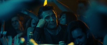 Movie still from “Taken 2” (2012), directed by Olivier Megaton – A man sitting at a table in front of other people; Close Up shot, Low angle