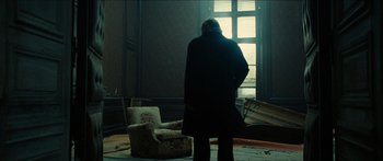 Movie still from “Taken 2” (2012), directed by Olivier Megaton – A person standing in a room with a chair and a window; Wide shot, Low angle
