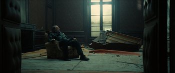 Movie still from “Taken 2” (2012), directed by Olivier Megaton – An old man sitting in a chair in a room; Wide shot, Low angle
