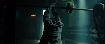 Movie still from “Taken 2” (2012), directed by Olivier Megaton – A man holding a barbell in a dark room; Medium shot, Low angle