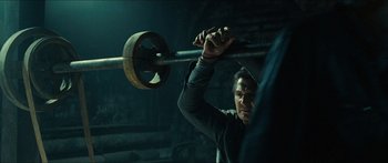 Movie still from “Taken 2” (2012), directed by Olivier Megaton – A man holding onto a barbell in a dark room; Medium shot, Low angle