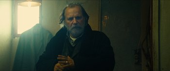 Movie still from “Taken 2” (2012), directed by Olivier Megaton – An old man with a beard is standing in a dark room; Close Up shot, Low angle