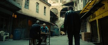 Movie still from “Taken 2” (2012), directed by Olivier Megaton – A group of people sitting at a table in an alleyway; Wide shot, Over the shoulder angle