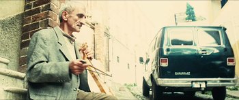 Movie still from “Taken 2” (2012), directed by Olivier Megaton – An older man sitting on the side of the road holding a guitar; Medium shot, Low angle