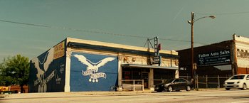 Movie still from “Taken 3” (2014), directed by Olivier Megaton – A car parked on the side of the road next to a building; Extreme Wide shot, Low angle