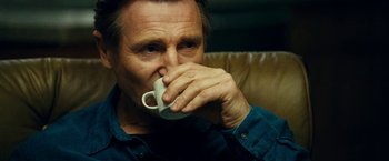 Movie still from “Taken 3” (2014), directed by Olivier Megaton – A man sitting on a couch drinking from a mug; Close Up shot, Low angle