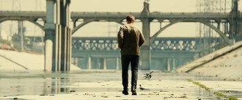 Movie still from “Taken 3” (2014), directed by Olivier Megaton – A man walking on the sidewalk near a bridge; Wide shot, Over the shoulder angle