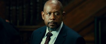 Movie still from “Taken 3” (2014), directed by Olivier Megaton – A man in a suit and tie in front of a book case; Close Up shot, Over the shoulder angle