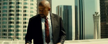 Movie still from “Taken 3” (2014), directed by Olivier Megaton – A man in a suit and tie standing in front of some buildings; Medium shot, Low angle