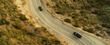 Movie still from “Taken 3” (2014), directed by Olivier Megaton – Two cars driving down a curvy road in the middle of the day; Extreme Wide shot, High angle