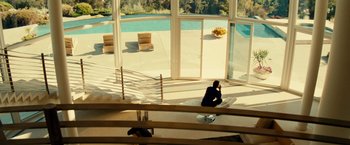 Movie still from “Taken 3” (2014), directed by Olivier Megaton – A woman sitting on a chair in a room with a swimming pool; Extreme Wide shot, High angle
