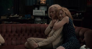 Movie still from “Only Lovers Left Alive” (2013), directed by Jim Jarmusch – Two women are sitting on a red couch and hugging; Medium shot, High angle