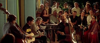 Movie still from “Talk to Her” (2002), directed by Pedro Almodóvar – A group of people sitting on a porch playing instruments; Wide shot, Over the shoulder angle