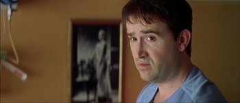 Movie still from “Talk to Her” (2002), directed by Pedro Almodóvar – A person in a room with a picture on the wall; Close Up shot, Over the shoulder angle