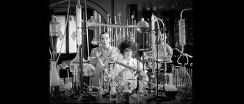 Movie still from “Talk to Her” (2002), directed by Pedro Almodóvar – A man and a woman standing in front of a table filled with glass; Medium shot, Low angle