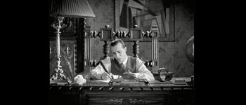 Movie still from “Talk to Her” (2002), directed by Pedro Almodóvar – A black and white photo of a man sitting at a desk writing; Medium shot, High angle