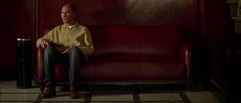 Movie still from “Talk to Her” (2002), directed by Pedro Almodóvar – A man sitting on top of a red couch; Wide shot, Low angle