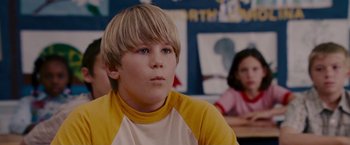 Movie still from “Talladega Nights: The Ballad of Ricky Bobby” (2006), directed by Adam McKay – A young boy sitting in front of a group of people; Close Up shot, Low angle