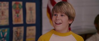 Movie still from “Talladega Nights: The Ballad of Ricky Bobby” (2006), directed by Adam McKay – A young boy smiles while standing in front of an american flag; Close Up shot, Low angle